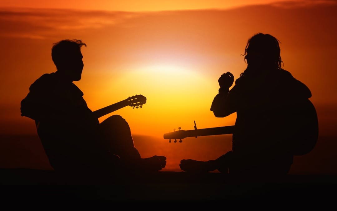 Two people sitting with musical instruments at sunset